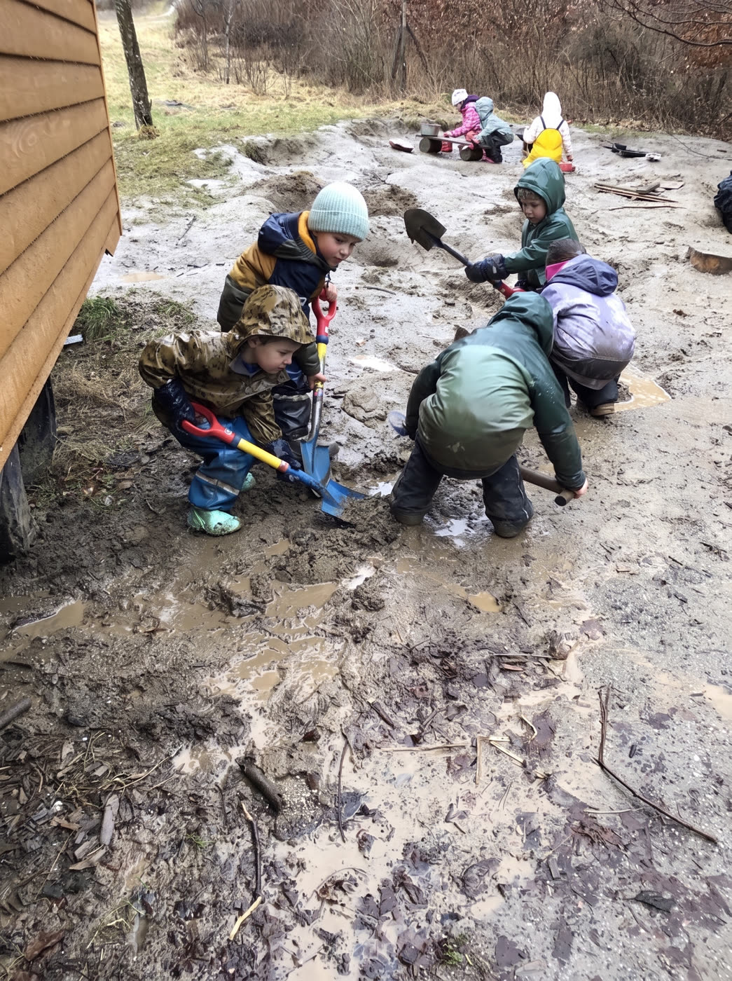 Kinder graben gemeinsam mit Schaufeln im Matsch am Bauwagen